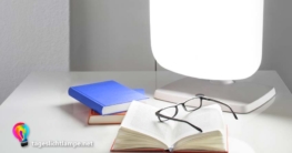 Tageslichtlampe auf Schreibtisch. Davor liegen zwei Bücher und eine Brille auf einem geöffneten Buch.